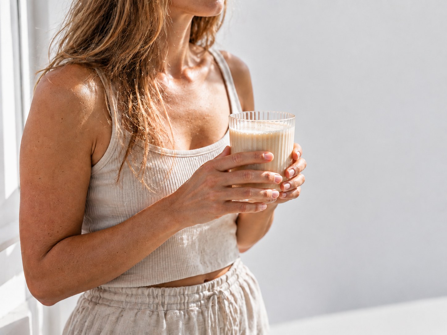 Woman by a window holding a glass of prepared Powerlogy Organic Whey Protein shake