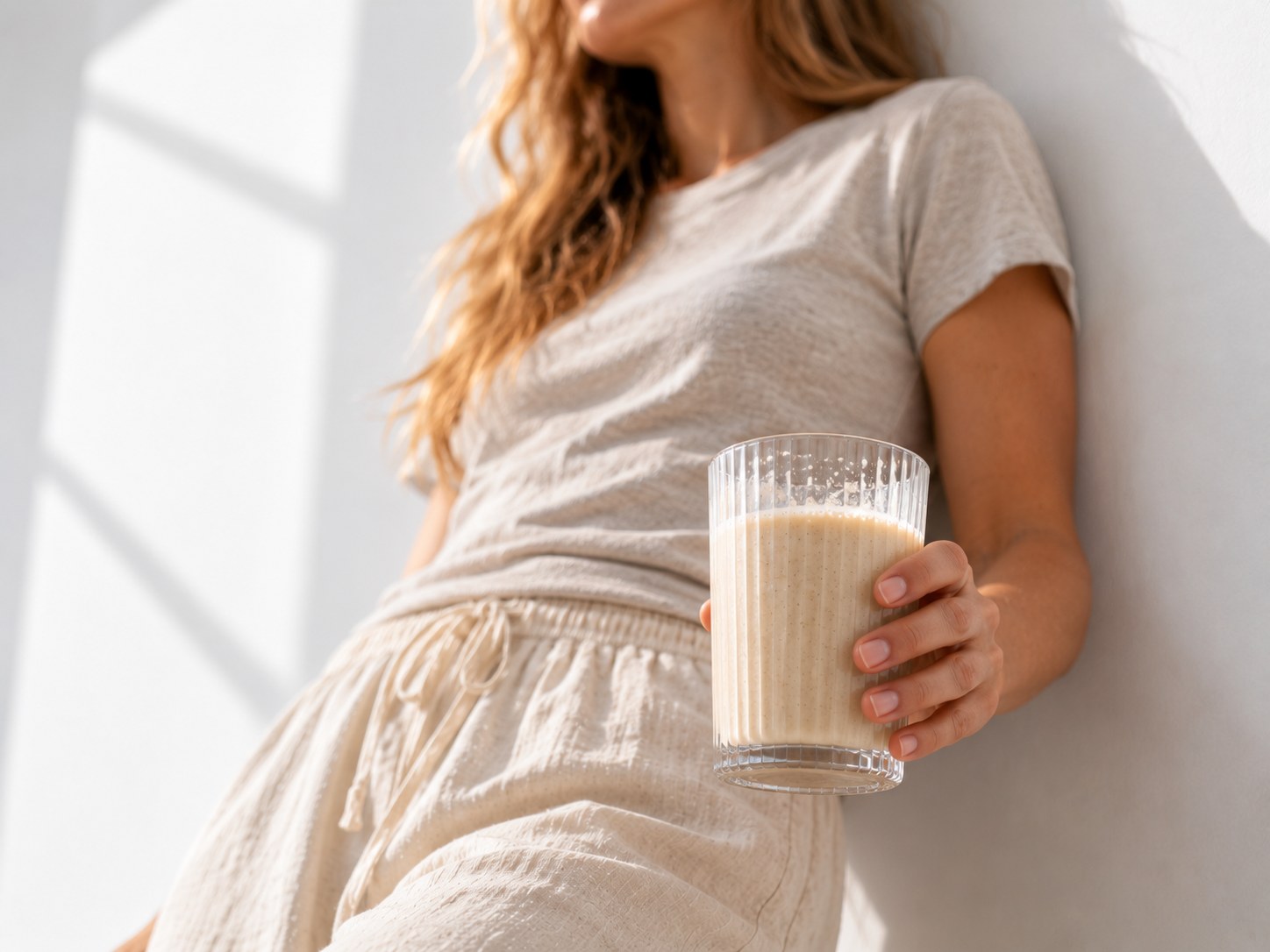 Žena stojí u stěny se sklenicí připraveného nápoje Powerlogy Organic Vegan Protein s příchutí skořice a vanilka