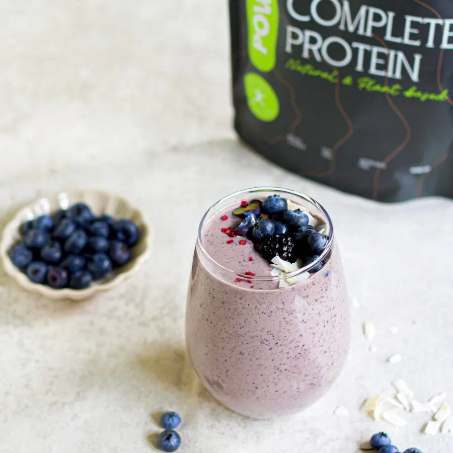 Violetter Heidelbeer-Smoothie in einem Glas, daneben frische Heidelbeeren und Chia-Samen