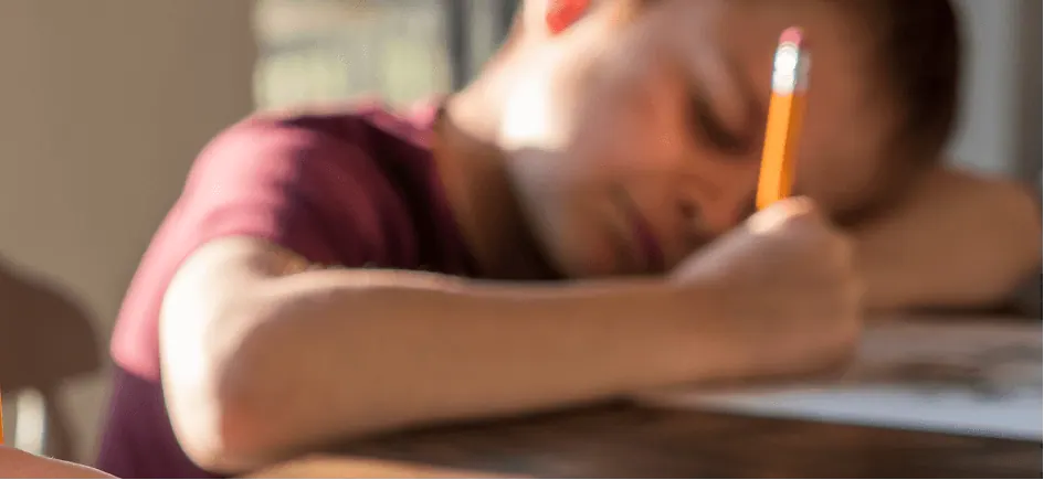 a tired pupil lying on a school desk and writing with a pencil