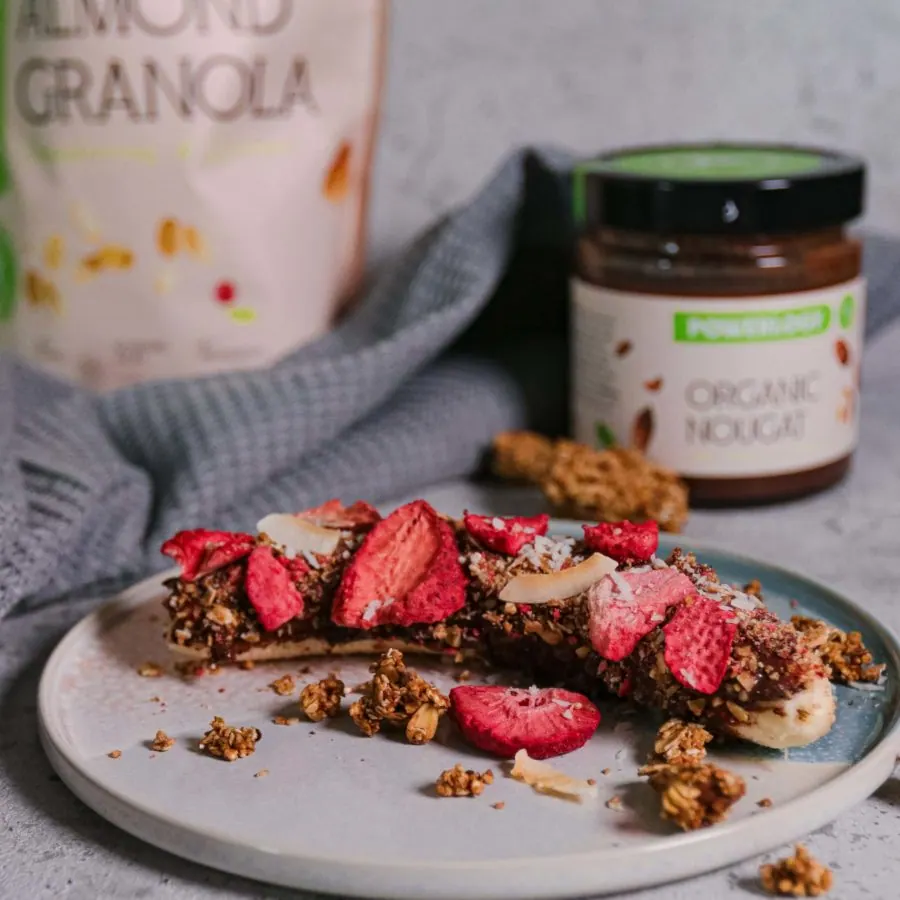 Halbierte Banane mit Nougat-Creme bestrichen, bestreut mit zerkleinertem Granola, gefriergetrockneten Erdbeeren und Kokosraspeln