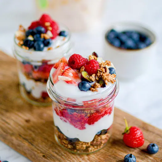 Schichtdessert im Glas aus Granola, weißem Joghurt und Waldfrüchten, mit Himbeeren und Heidelbeeren getoppt