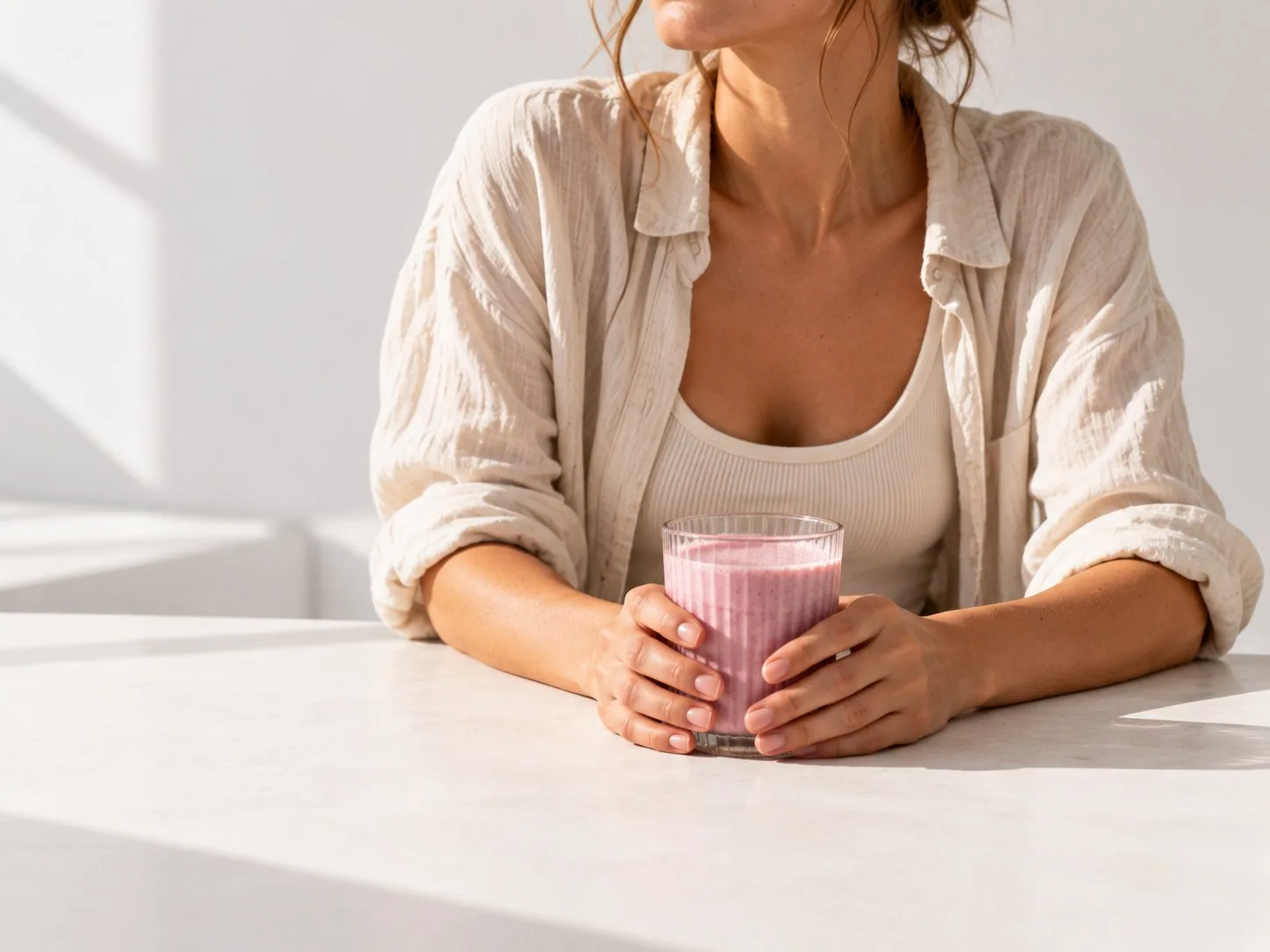 Woman sitting at a table with a glass of prepared Powerlogy Whey Protein Berries shake